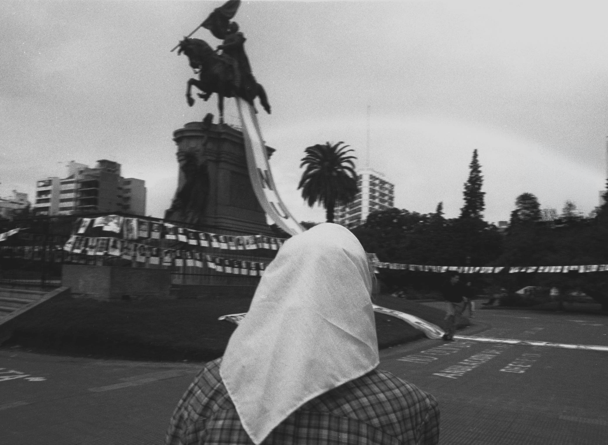 Una Madre de Plaza de Mayo frente al monumento, con la valla de fotos de los desaparecidos.
